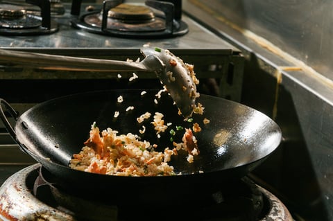 A chef skillfully tossing fried rice in a wok on a stovetop, capturing the motion and vibrant colors