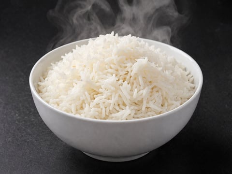 Steaming white rice in a white bowl on dark surface