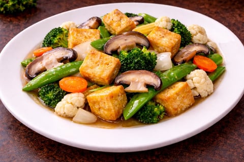 Stir-fried tofu and vegetable dish with broccoli, mushrooms, snap peas, and carrots on a white plate