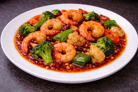 Stir-fried shrimp and broccoli served on a white plate with red sauce and garnishes