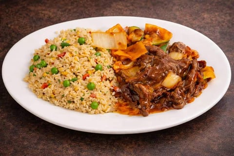 Plate of fried rice with peas and carrots, roasted potatoes, and braised beef on white plate