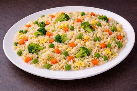 A white plate of vegetable fried rice with broccoli, carrots, peas, and corn on a dark surface