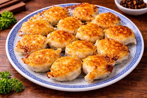 Golden-brown pan-fried dumplings arranged on a blue and white plate with garnish and condiments on a wooden surface