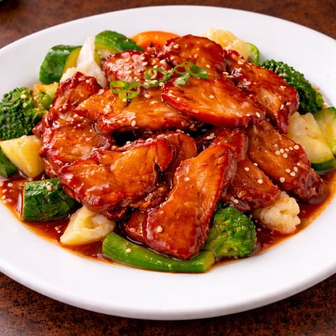 Glazed chicken pieces with sesame seeds served over broccoli, pineapple, and peppers on a white plate