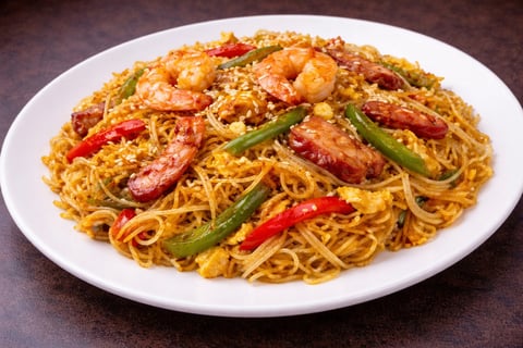 Asian stir-fried noodle dish with shrimp, sliced red peppers, green onions, and sesame seeds served on a white plate