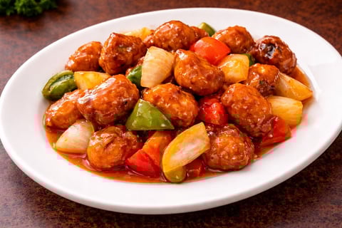Plate of glazed meatballs with red peppers, pineapple, and green peppers on white plate