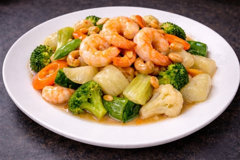 Shrimp stir-fry with cashews, broccoli, carrots, and water chestnuts served on a white plate