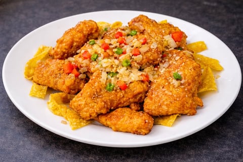 Crispy fried chicken pieces topped with diced vegetables served on a bed of golden fries on a white plate