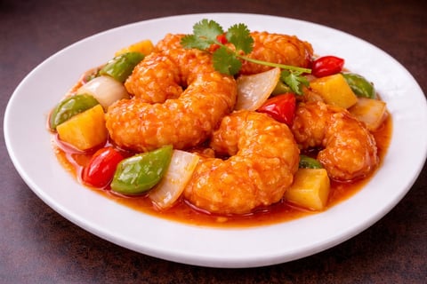 Plate of glazed orange shrimp with red peppers, pineapple chunks, and cilantro garnish on a white plate