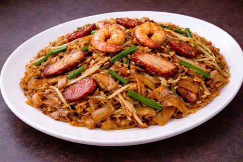 Asian noodle dish with shrimp, sliced sausage, and green onions served on a white plate